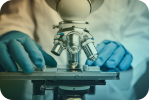 The gloved hands of a scientist position a slide under a compound microscope.