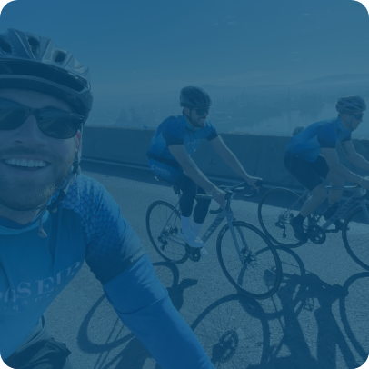 Three employees wearing Poseida shirts, helmets, and sunglasses, smile while riding bikes. The image is tinted blue.