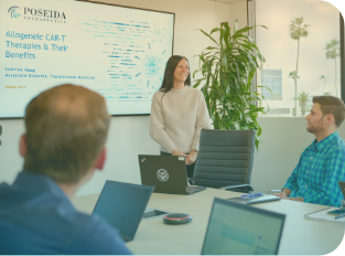 A Poseida employee stands at the front of a full conference room presenting slides displayed on a screen. Several employees sitting around the conference table look at the slides.